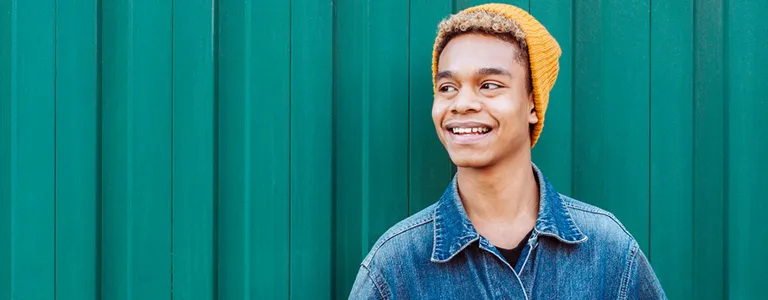 male student standing against wall smiling